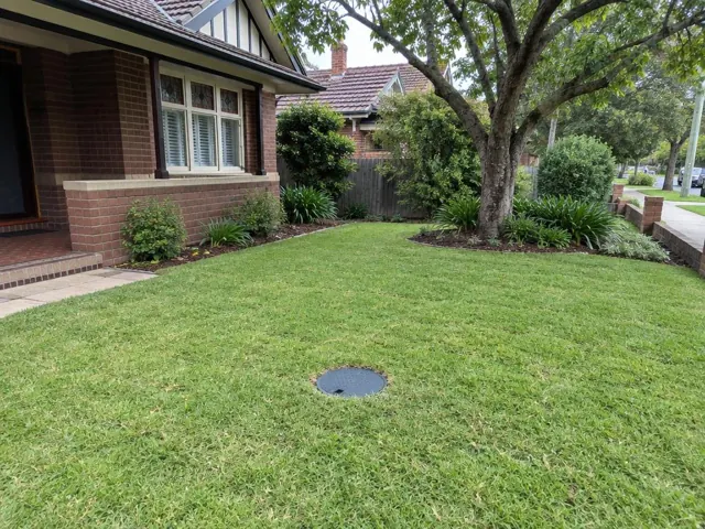 Circular capped opening in a grassy front yard beside a brick house in Normanhurst